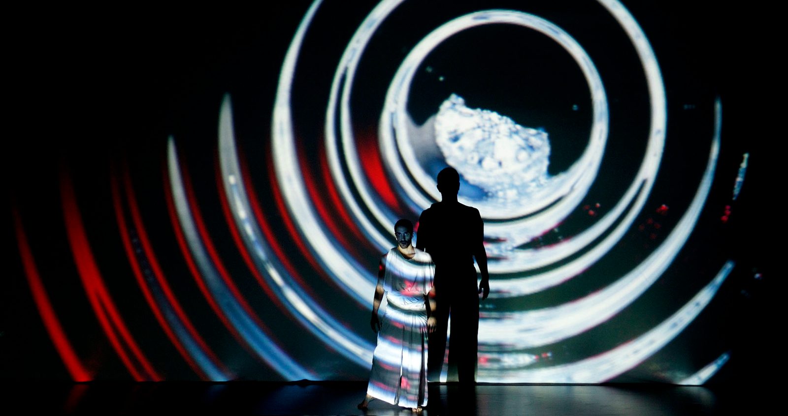 Two performers within a circular red, white and black projection