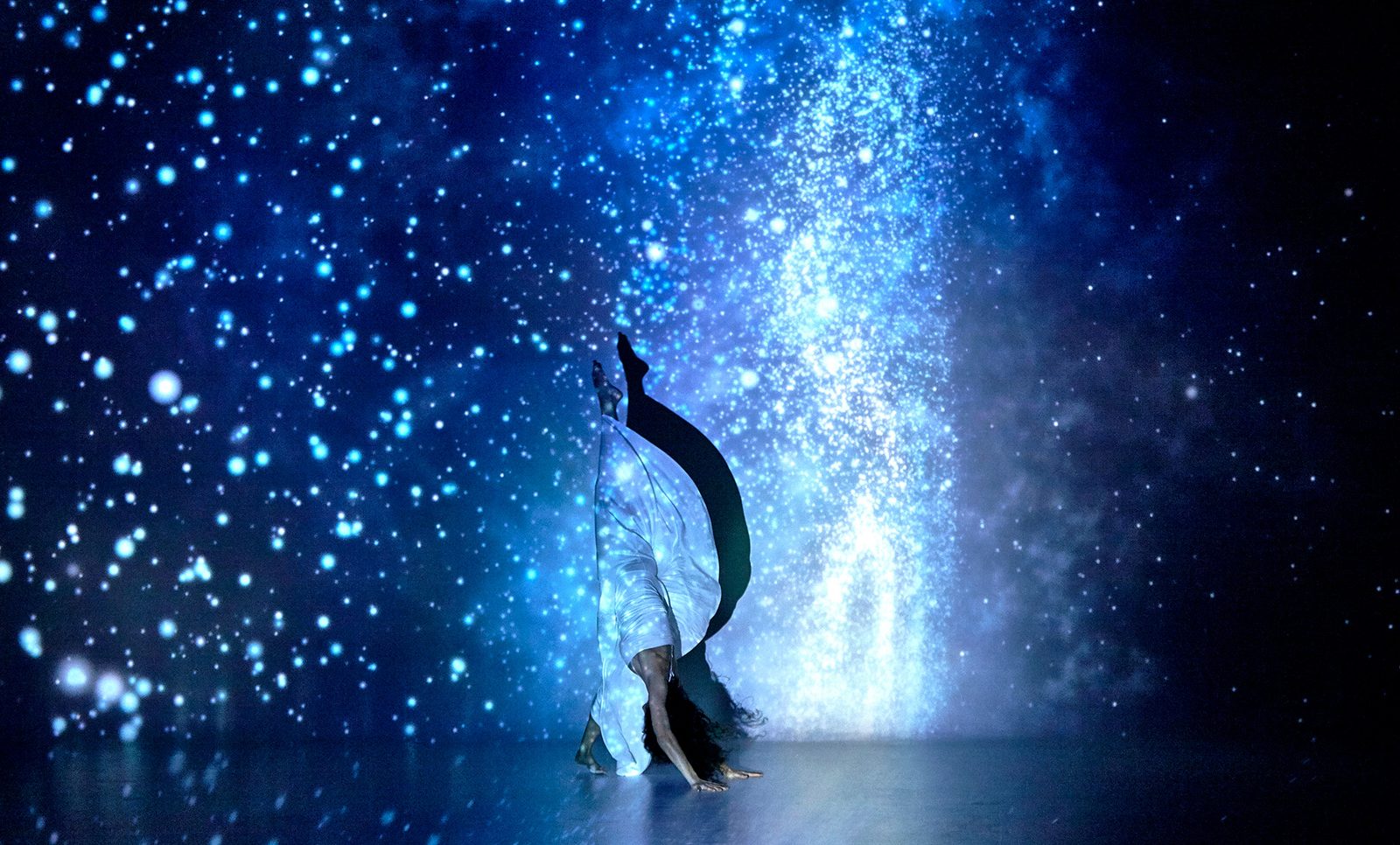 A dancer inverted beneath a field of projected stars