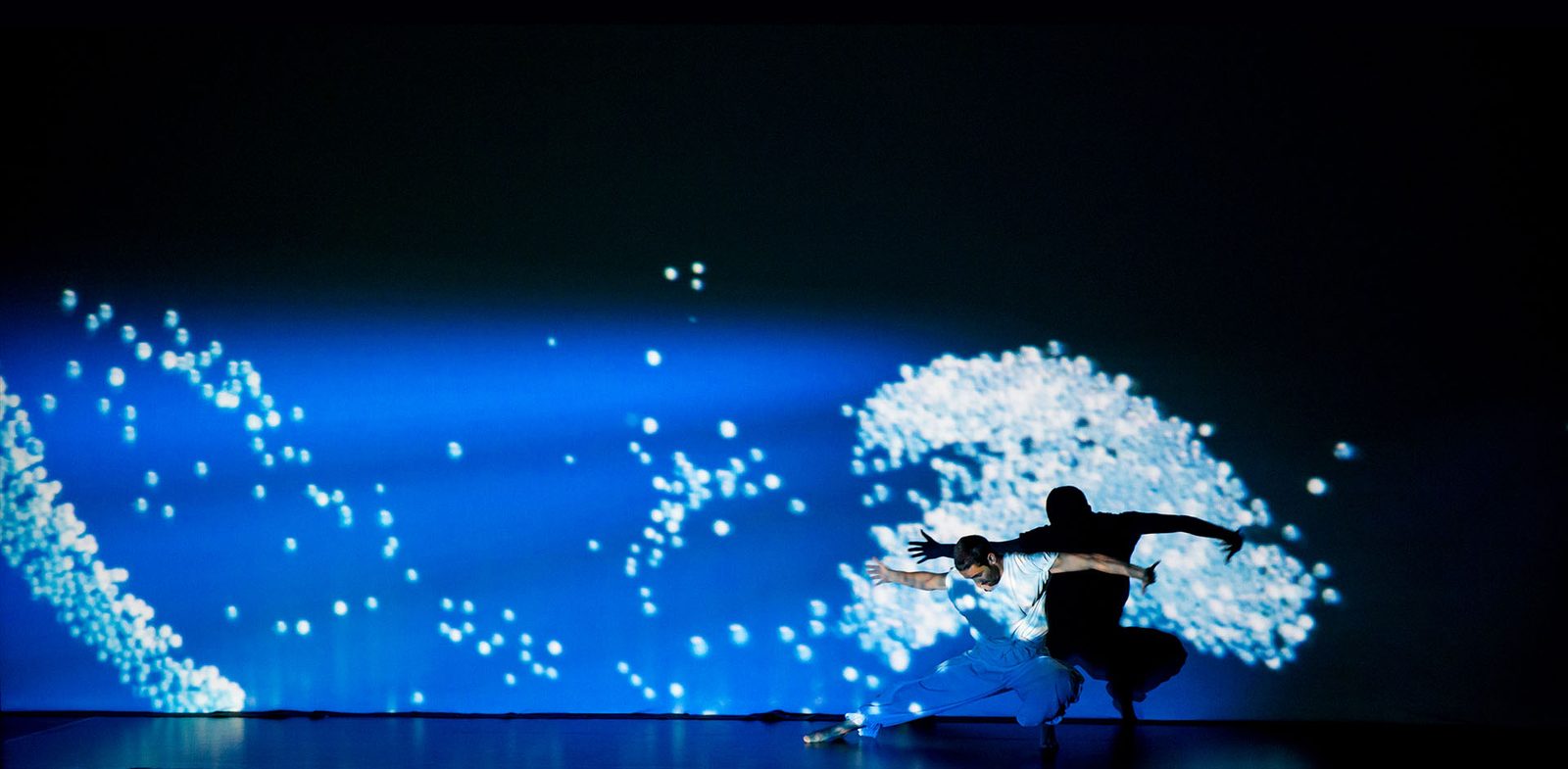 Two dancers extending across a deep-blue digital image